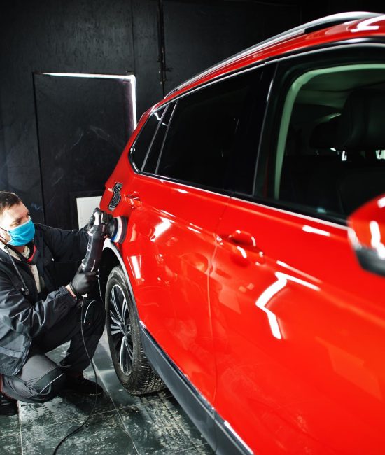 car-detailing-concept-man-face-mask-with-orbital-polisher-repair-shop-polishing-orange-suv-car